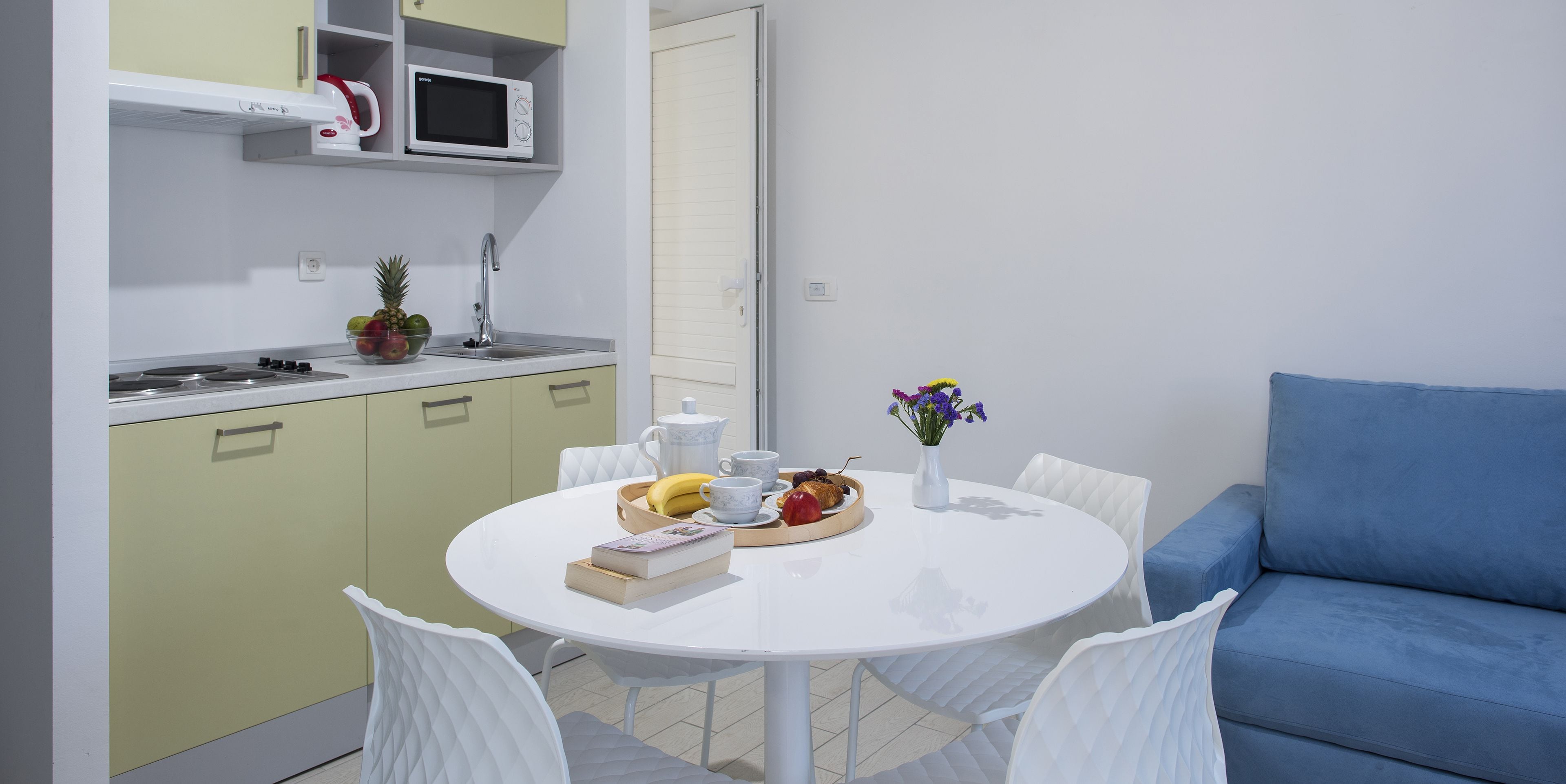 A modern kitchen with a white table, chairs, and a blue sofa.