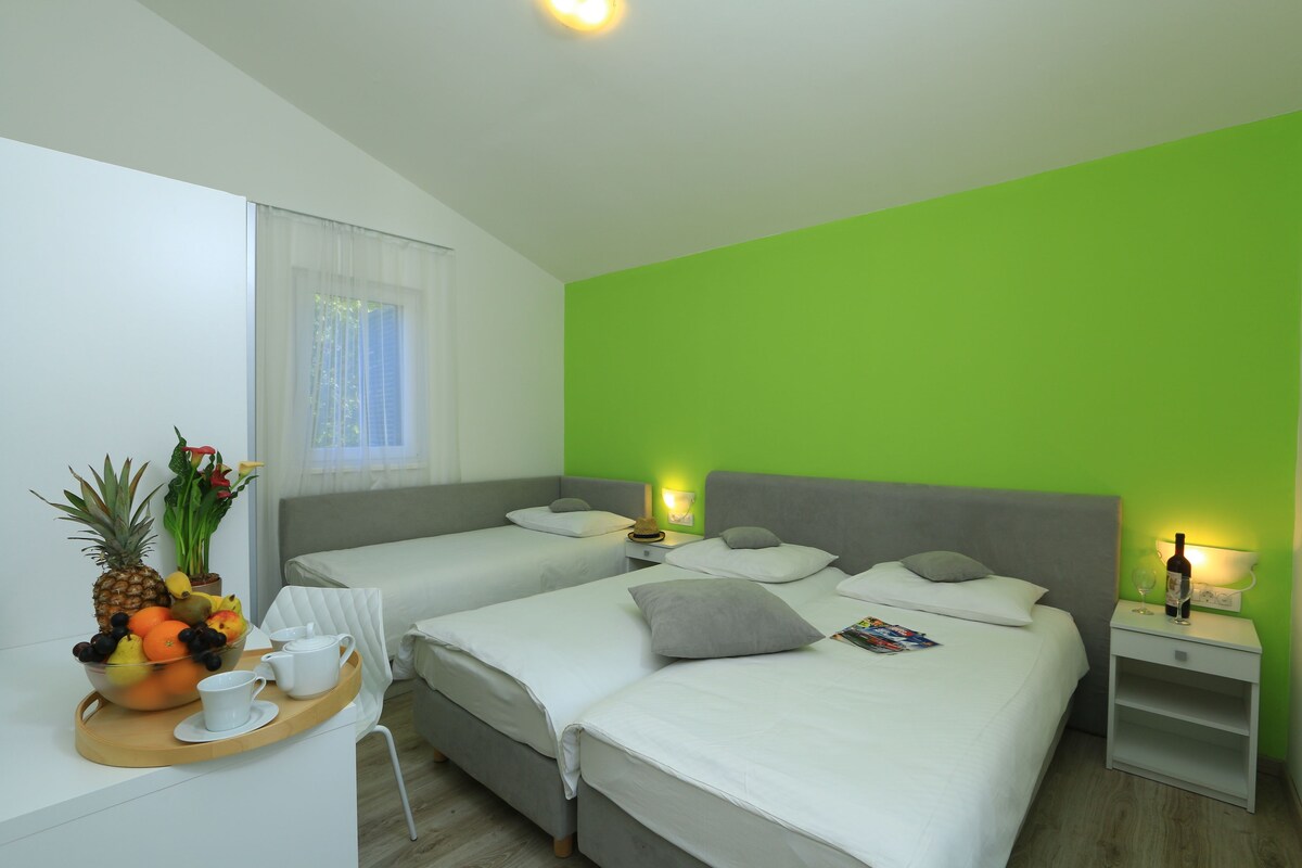 A hotel room with two beds, a breakfast tray with fruit and coffee, and a green accent wall.