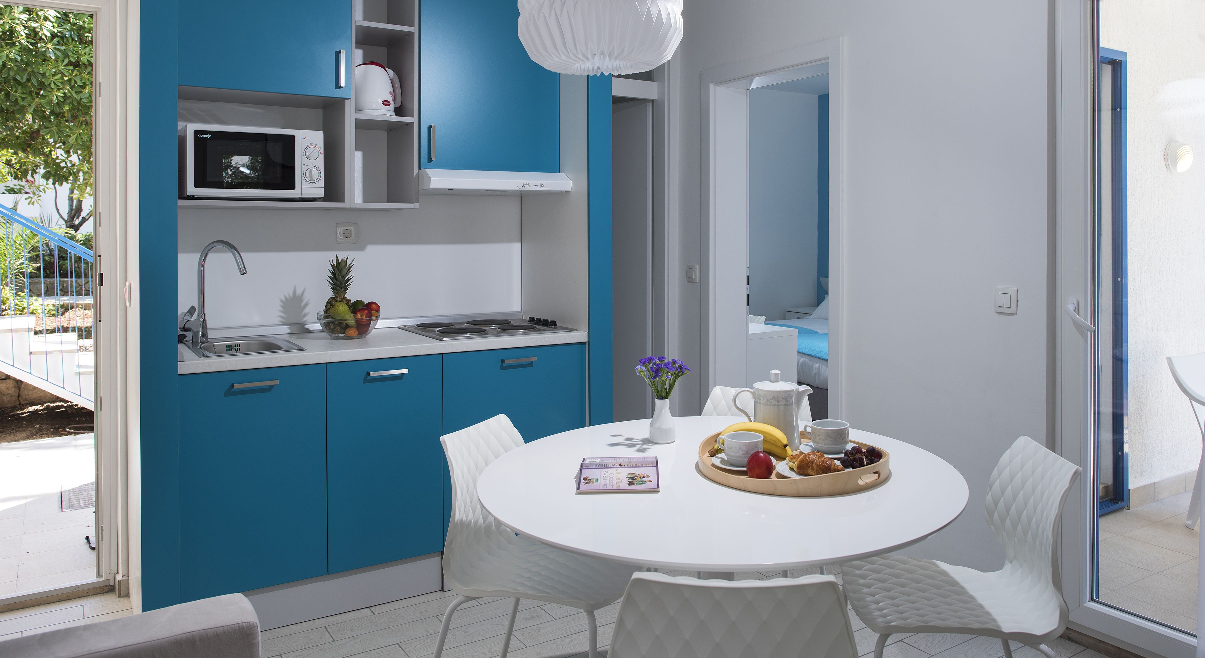 Eine moderne Küche mit blauen Schränken, einer weißen Arbeitsplatte und einem Essbereich mit einem weißen Tisch und Stühlen.