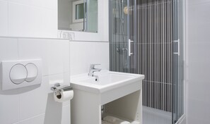 Un baño moderno con un lavamanos blanco, una cabina de ducha con mampara de vidrio y un dispensador de papel higiénico.