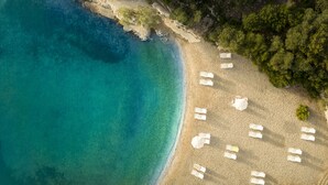 Vista aérea de una playa con aguas turquesas cristalinas, orilla de arena y sillones blancos dispuestos a lo largo de la costa.