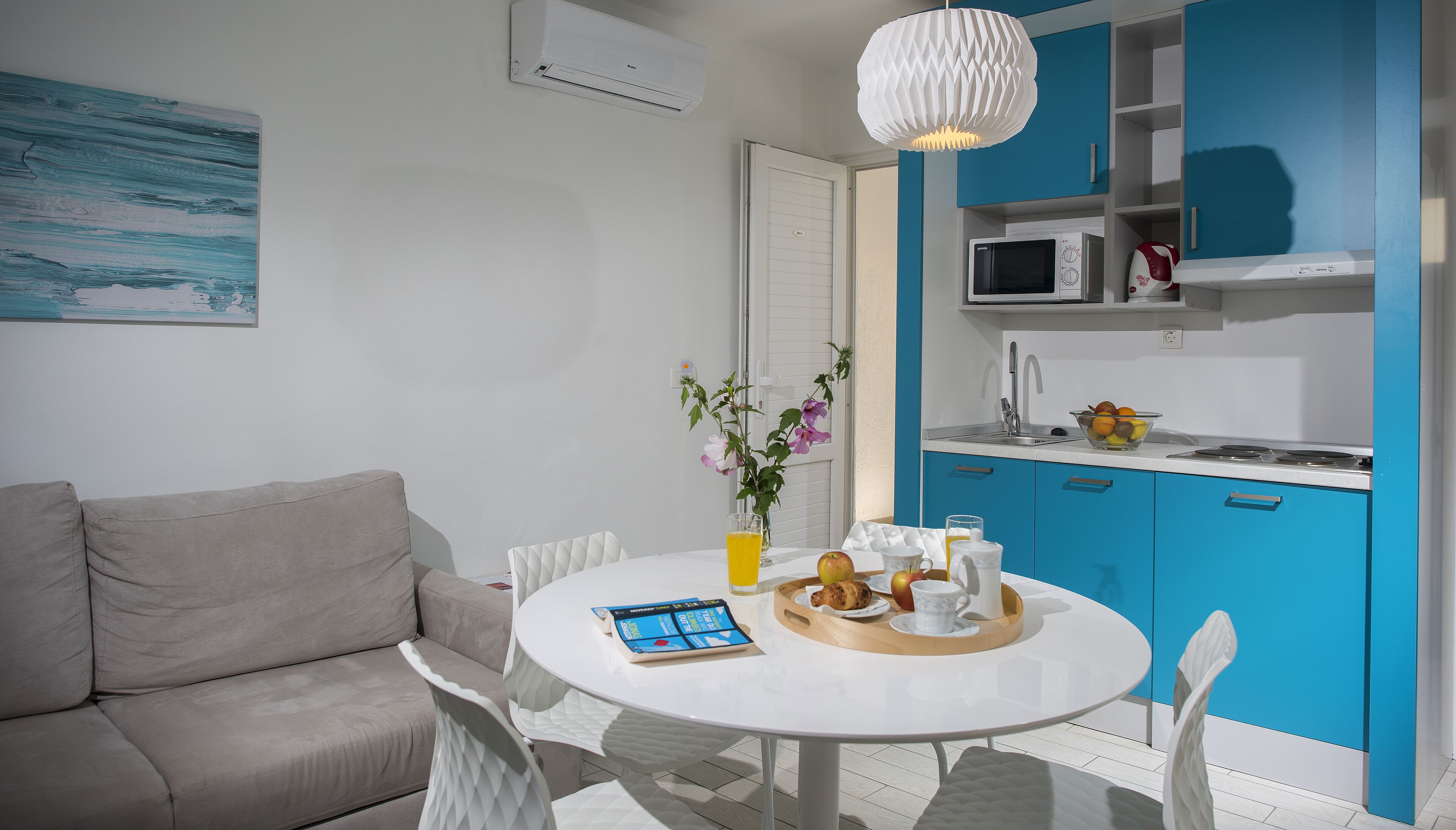 A modern kitchen with blue cabinets, a white countertop, and a dining area with a white table and chairs.