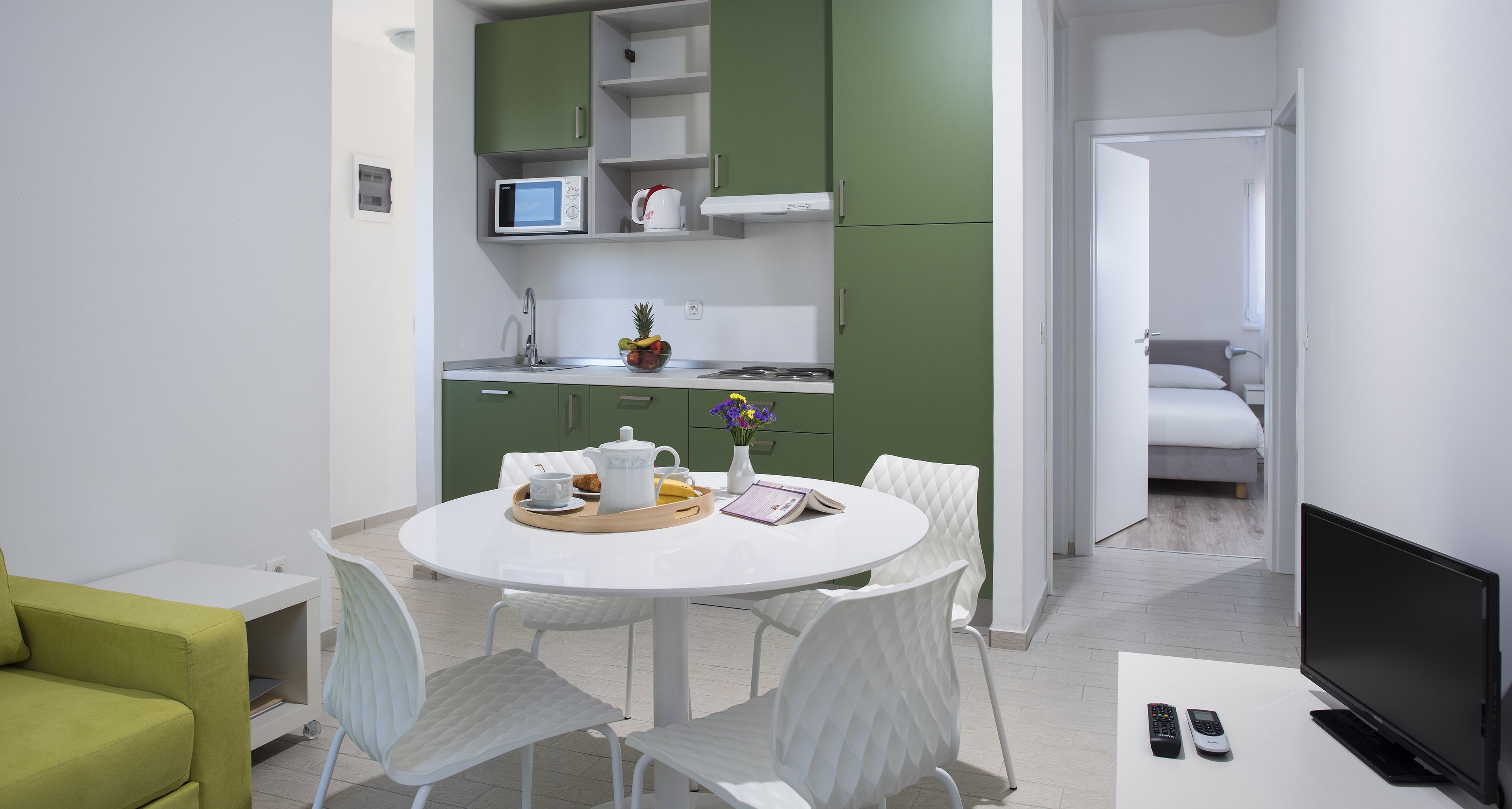 A modern kitchen with green cabinets, a dining table with chairs, and a TV on a stand.