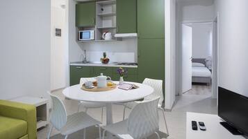 A modern kitchen with green cabinets, a dining table with chairs, and a TV on a stand.