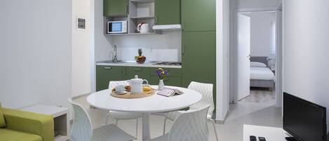 A modern kitchen with green cabinets, a dining table with chairs, and a TV on a stand.