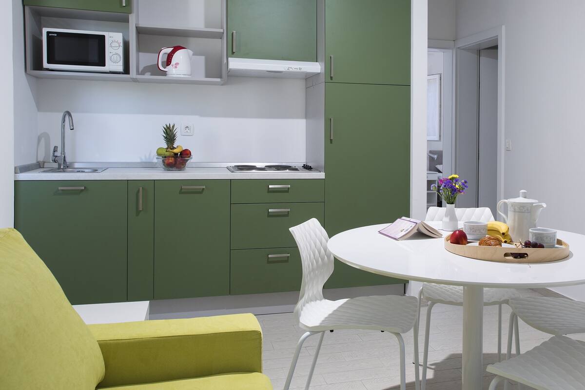 A modern kitchen with green cabinets, a white countertop, and a dining area with a white table and chairs.