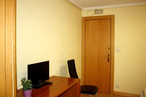 Una habitación con un escritorio de madera, una silla, un televisor y una puerta.