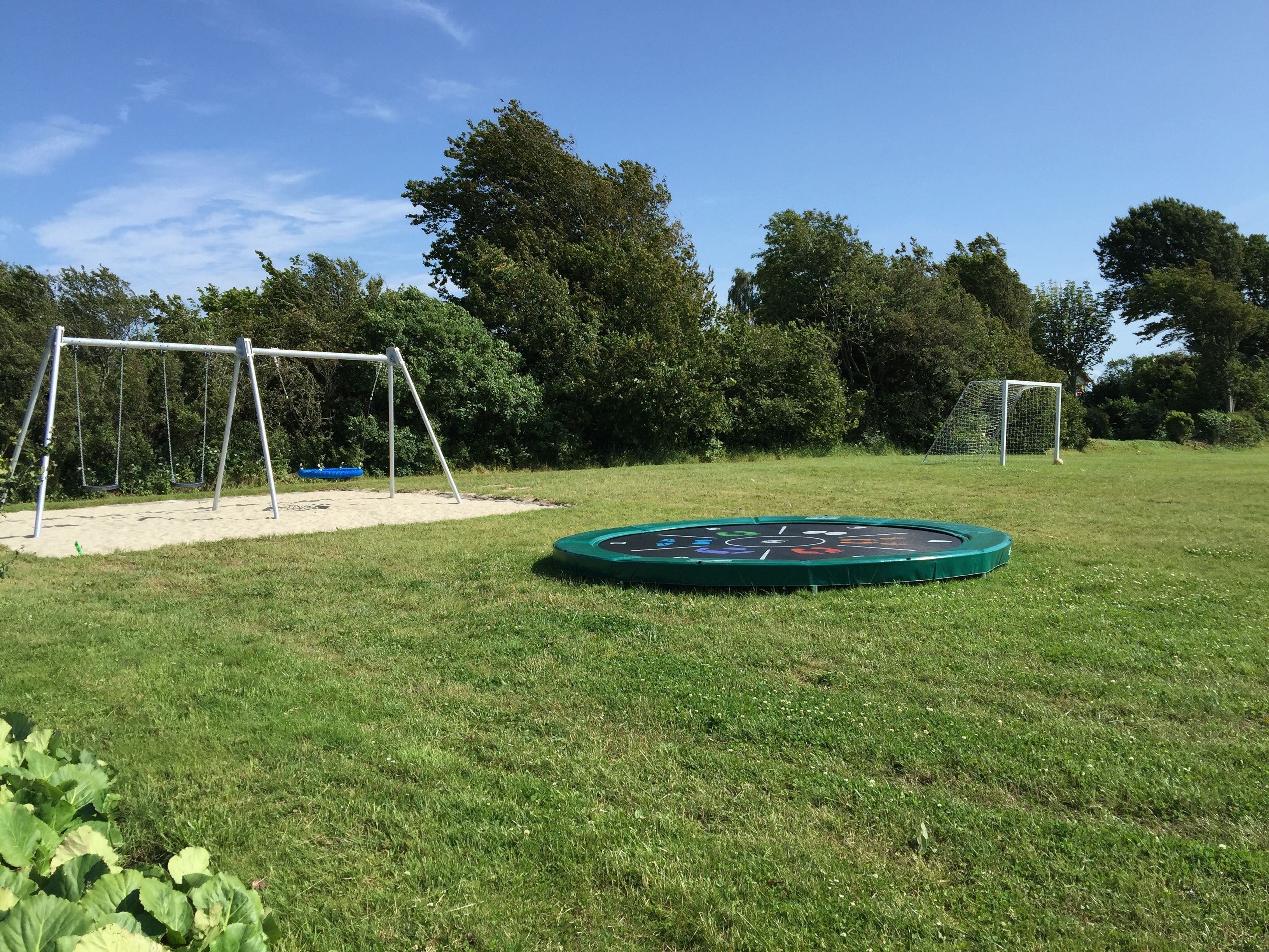 Un espacio al aire libre con césped, un columpio, un trampolín y una portería de fútbol.