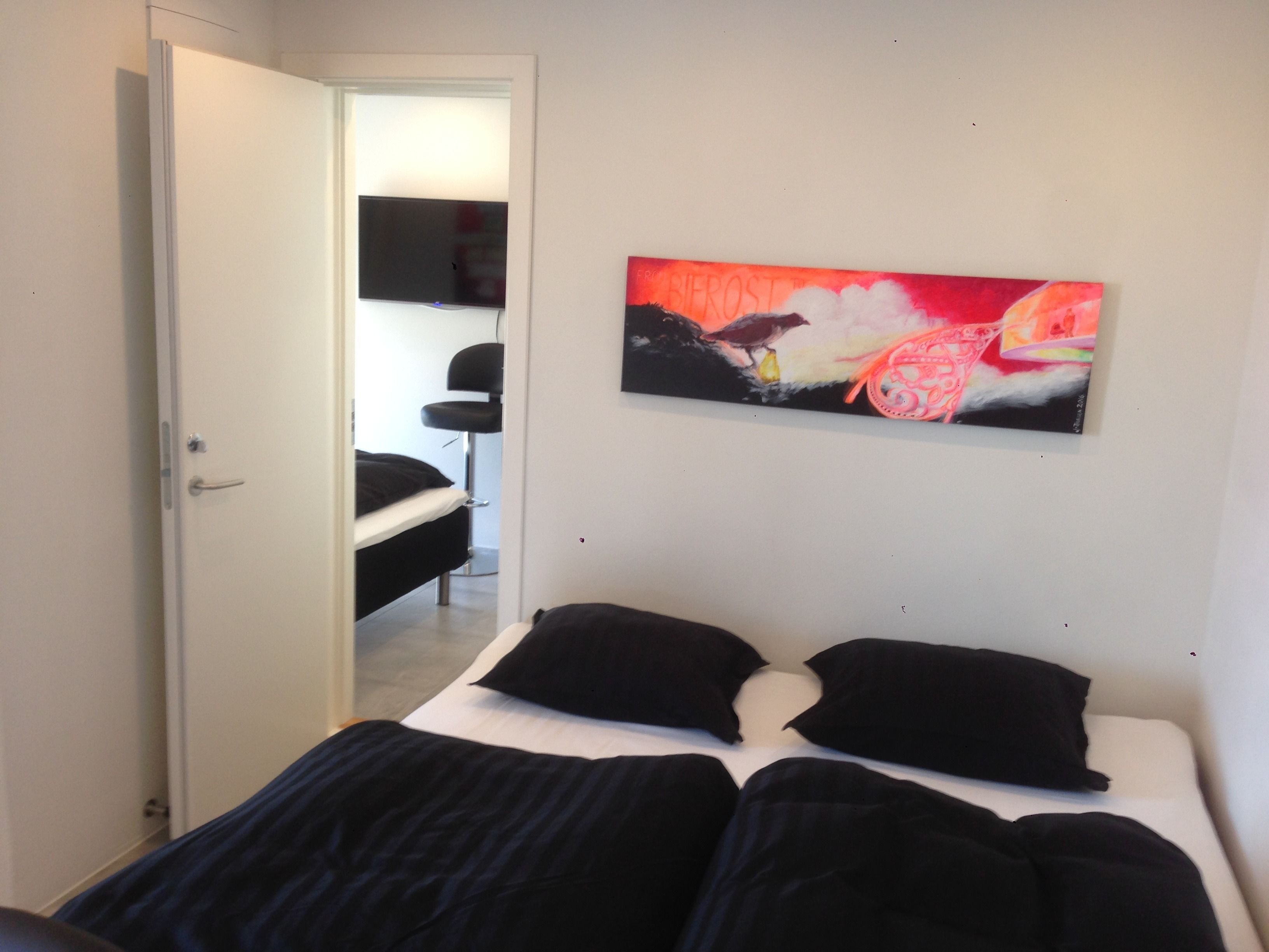 Ein Schlafzimmer mit einem Bett, einem Gemälde und einem Fernseher im angrenzenden Raum.