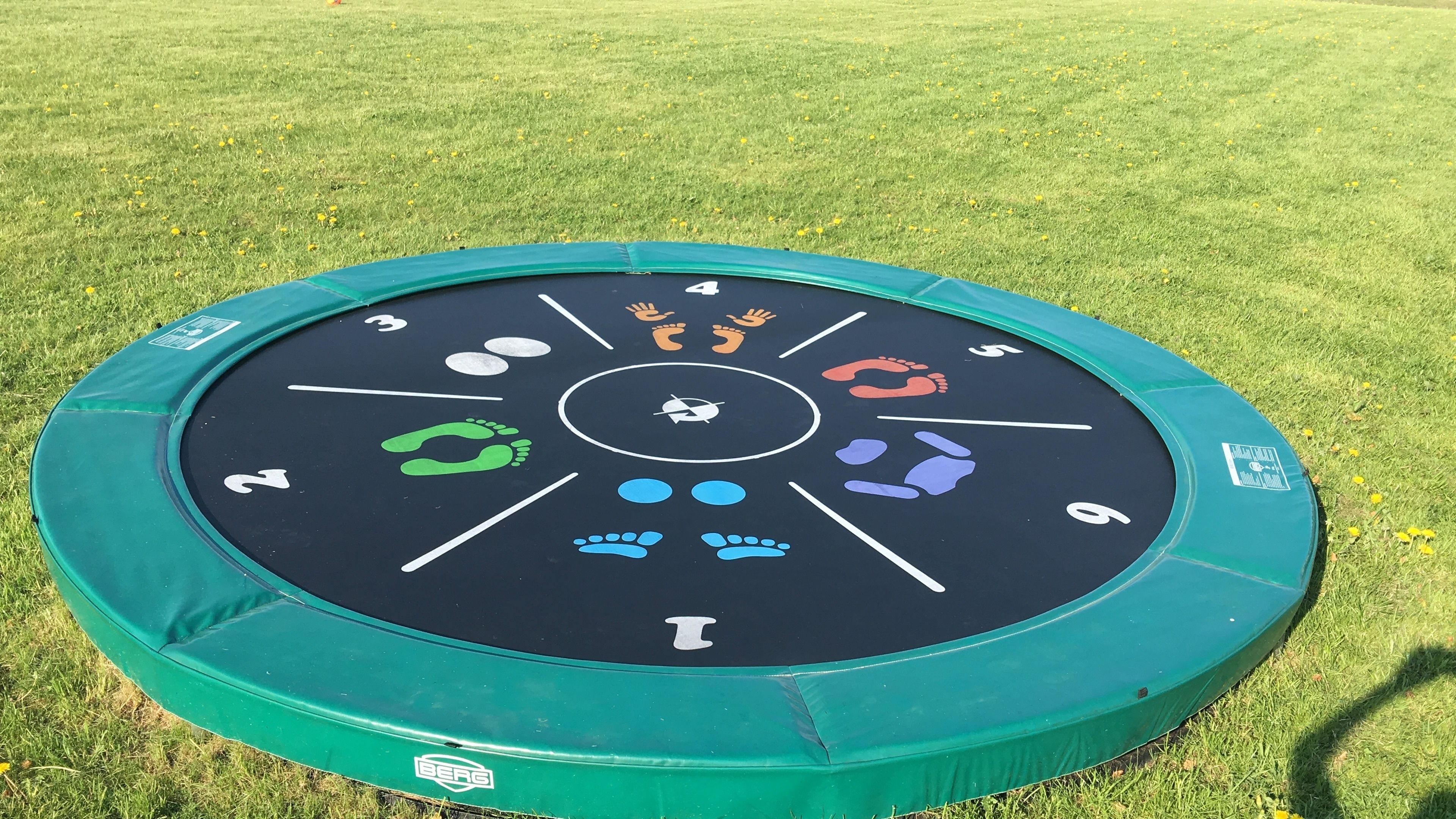 A circular outdoor activity mat with numbered sections and footprints, surrounded by grass.