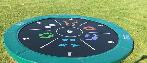A circular outdoor activity mat with numbered sections and footprints, surrounded by grass.