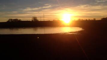 A sunset over a body of water with a silhouette of trees and a power line structure.