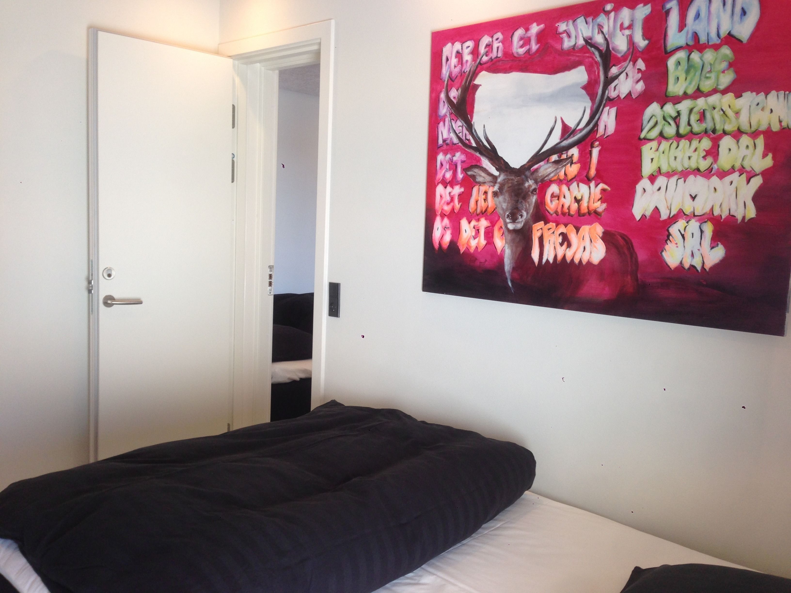 Ein Schlafzimmer mit einem Bett, einer Tür und einer Wand mit einem farbenfrohen Gemälde.
