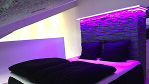 A bedroom with a stone headboard, two black beds with white linens, and a sloped ceiling. - Elisesminde (Vejle)