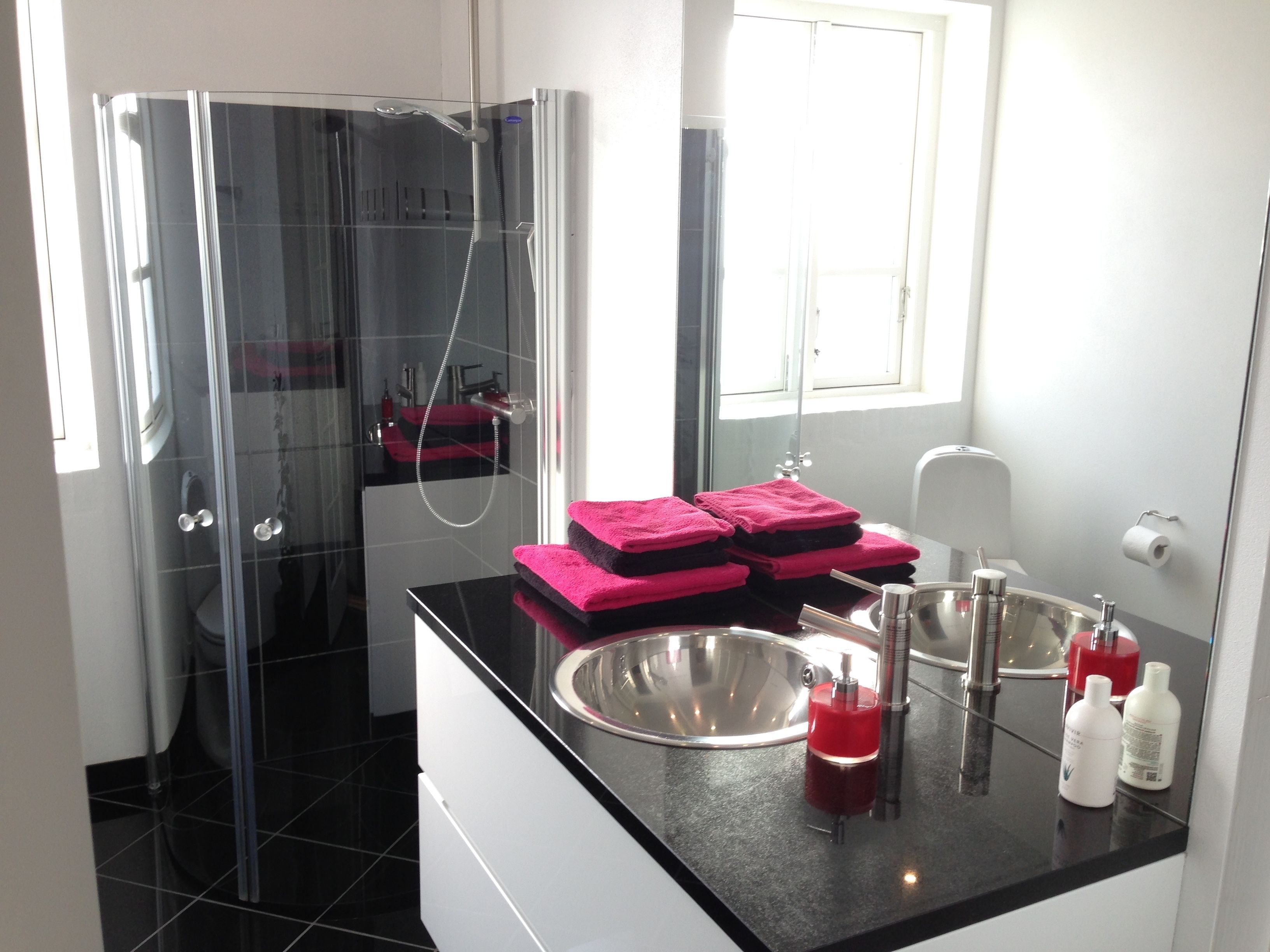 A modern bathroom with a glass-enclosed shower, a black countertop, and pink towels.