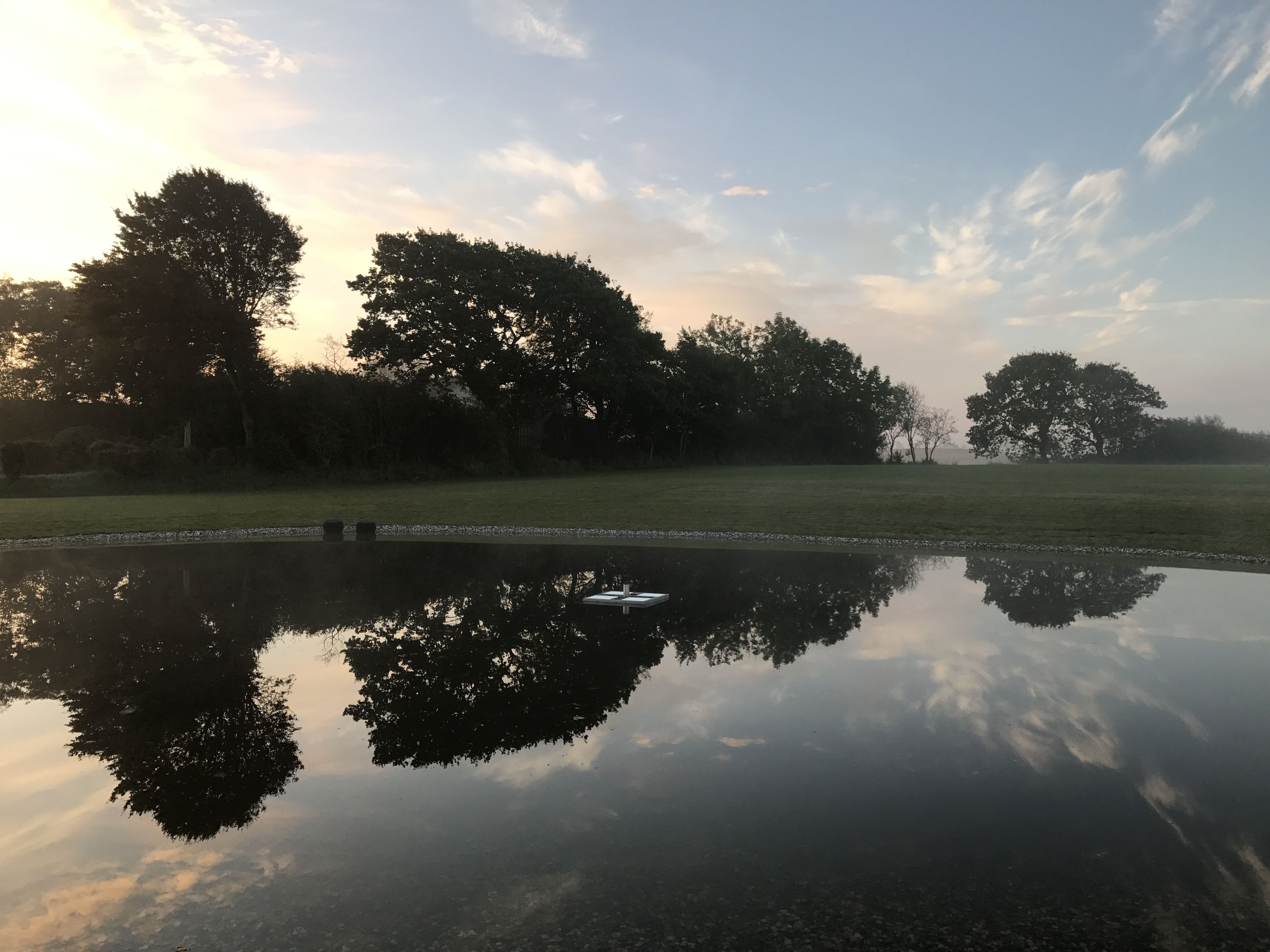 Stille vand spejler træer og en klar himmel.