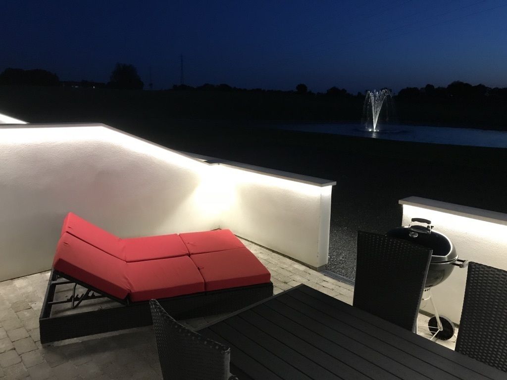 An outdoor patio with a red cushioned seating area, a grill, and a fountain in the background.