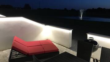 An outdoor patio with a red cushioned seating area, a grill, and a fountain in the background.