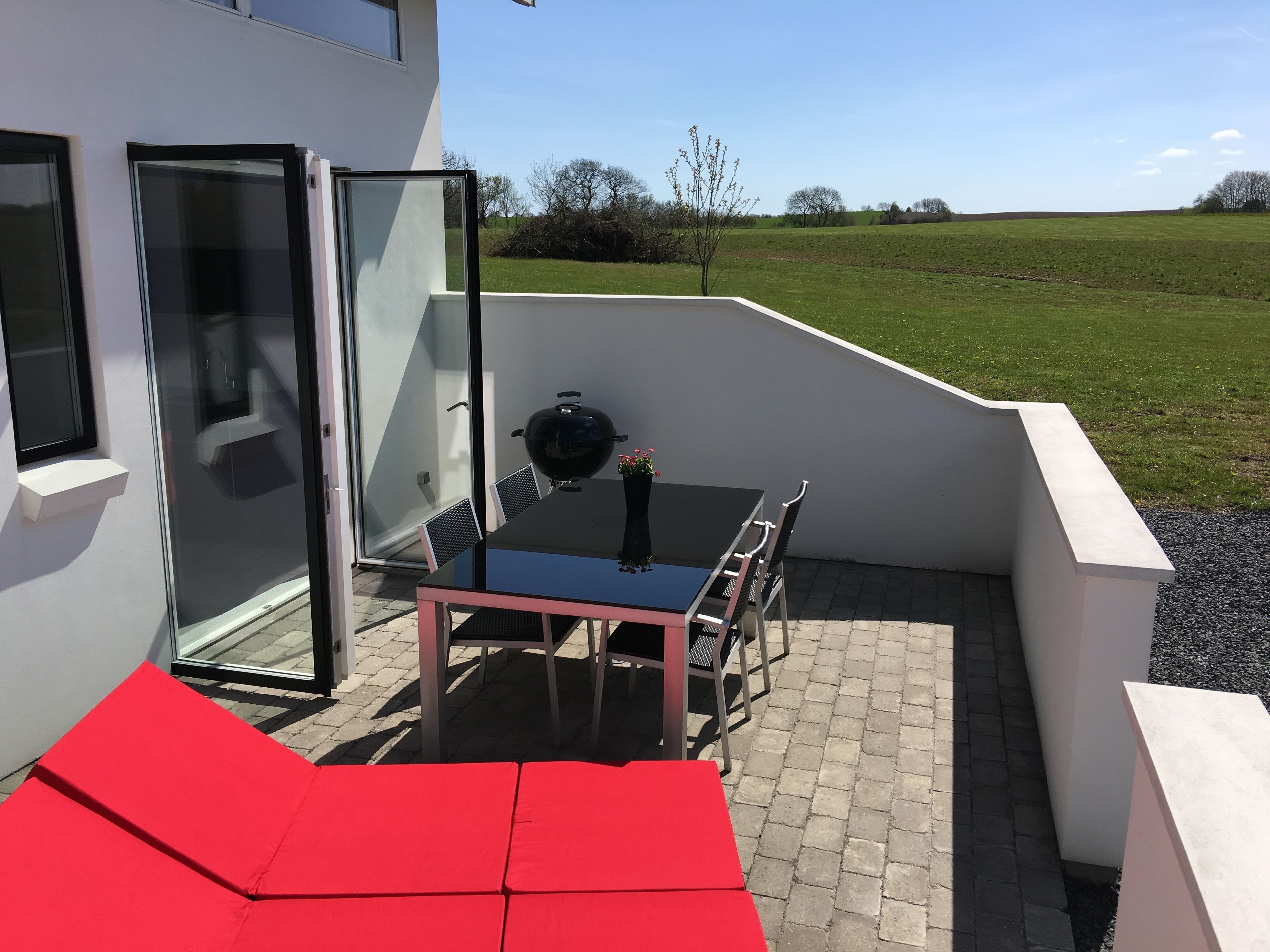 Eine Terrassenausstattung mit Tisch, Stühlen, einem Grill und einem roten Sofa.