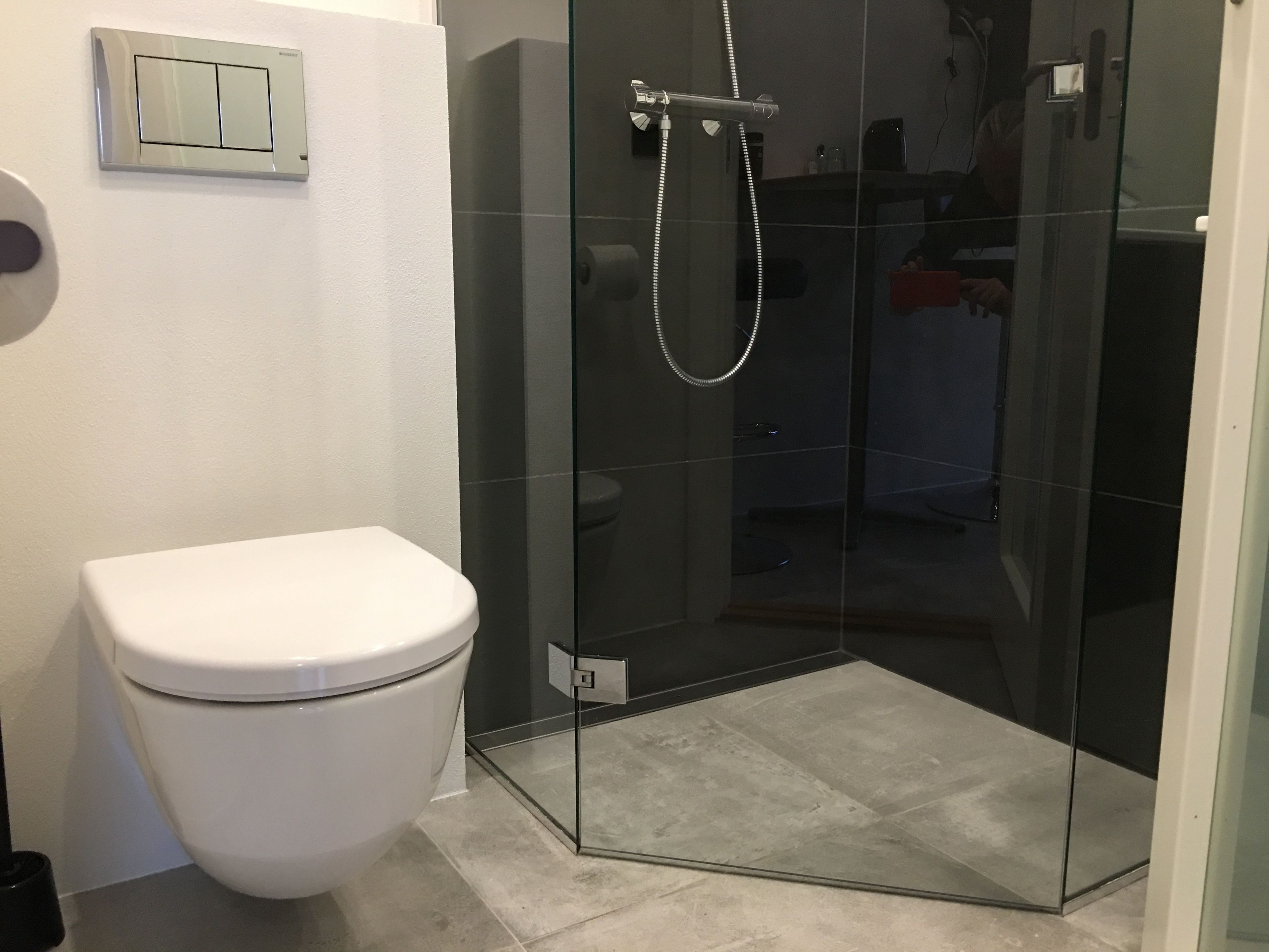 Ein modernes Badezimmer mit Toilette, einer Dusche mit Glasabtrennung und einem Lichtschalter an der Wand.