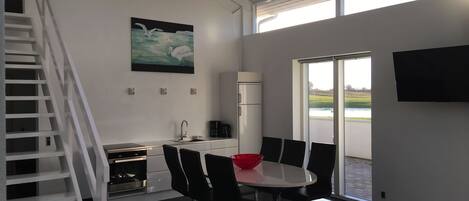 A modern kitchen with a dining area, a staircase, and a large window offering a view of the outdoors.