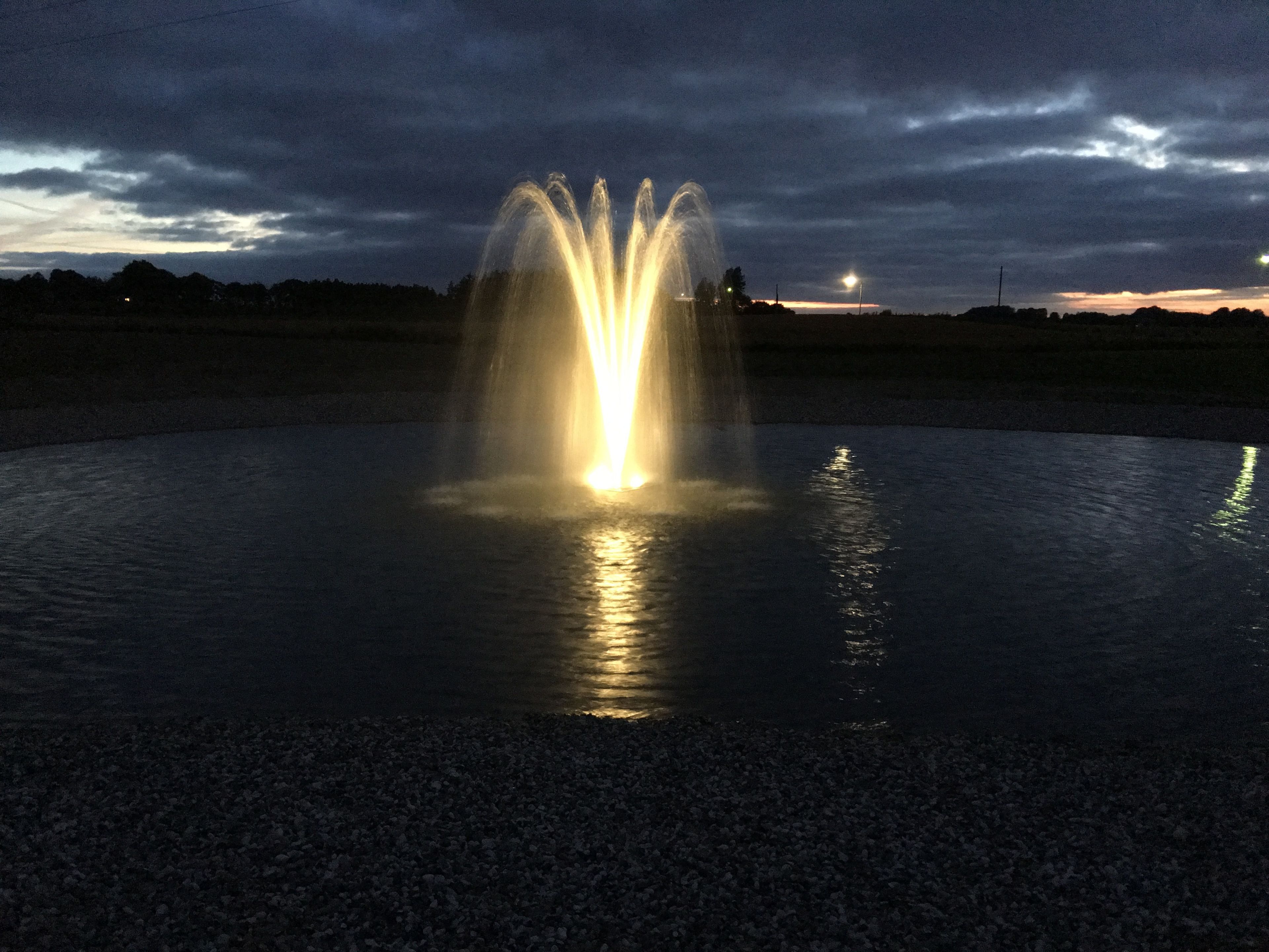 A fountain at night with water jets illuminated by lights, reflecting on the water surface.