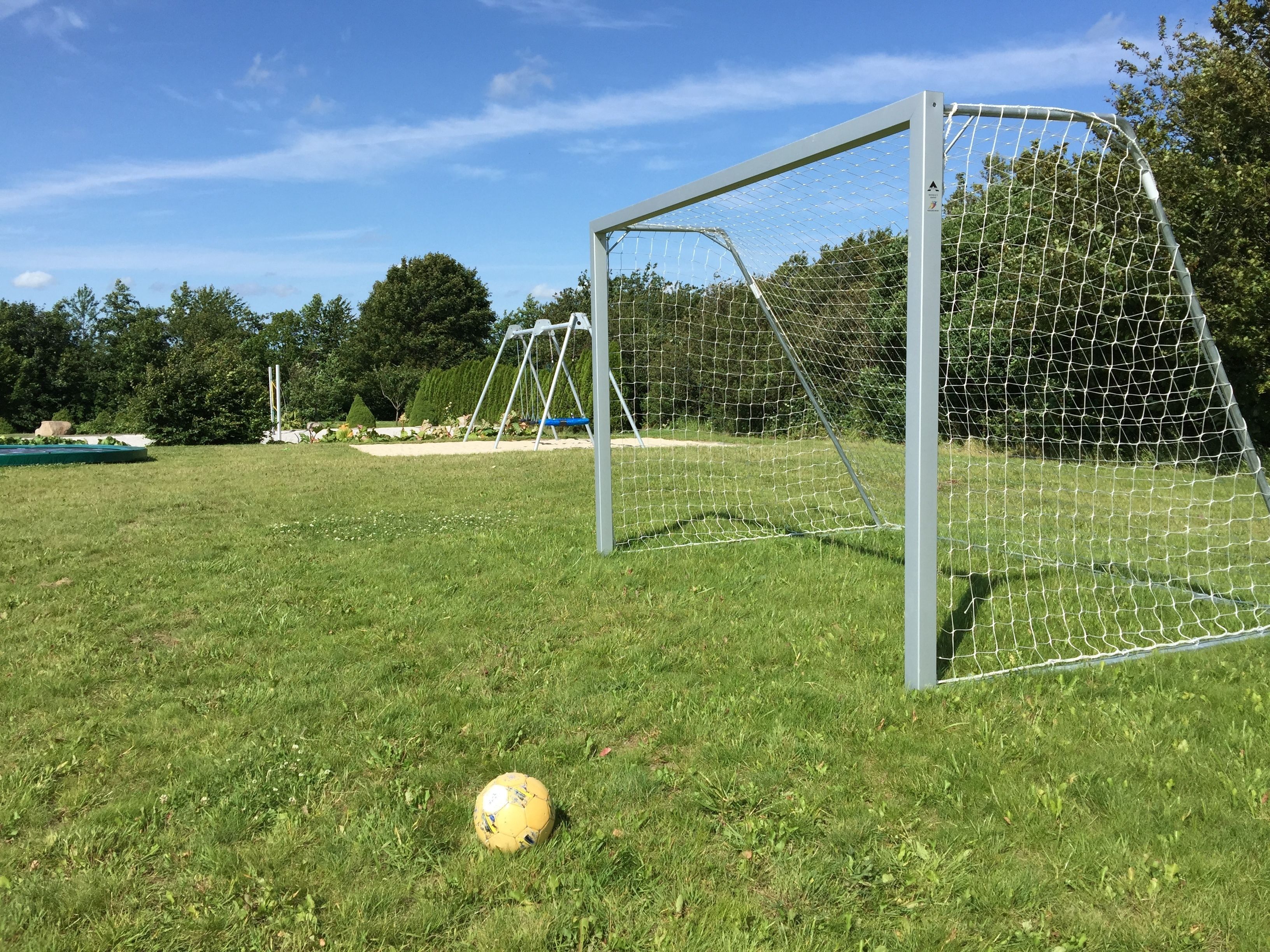 A soccer goal in a grassy field with trees in the background.