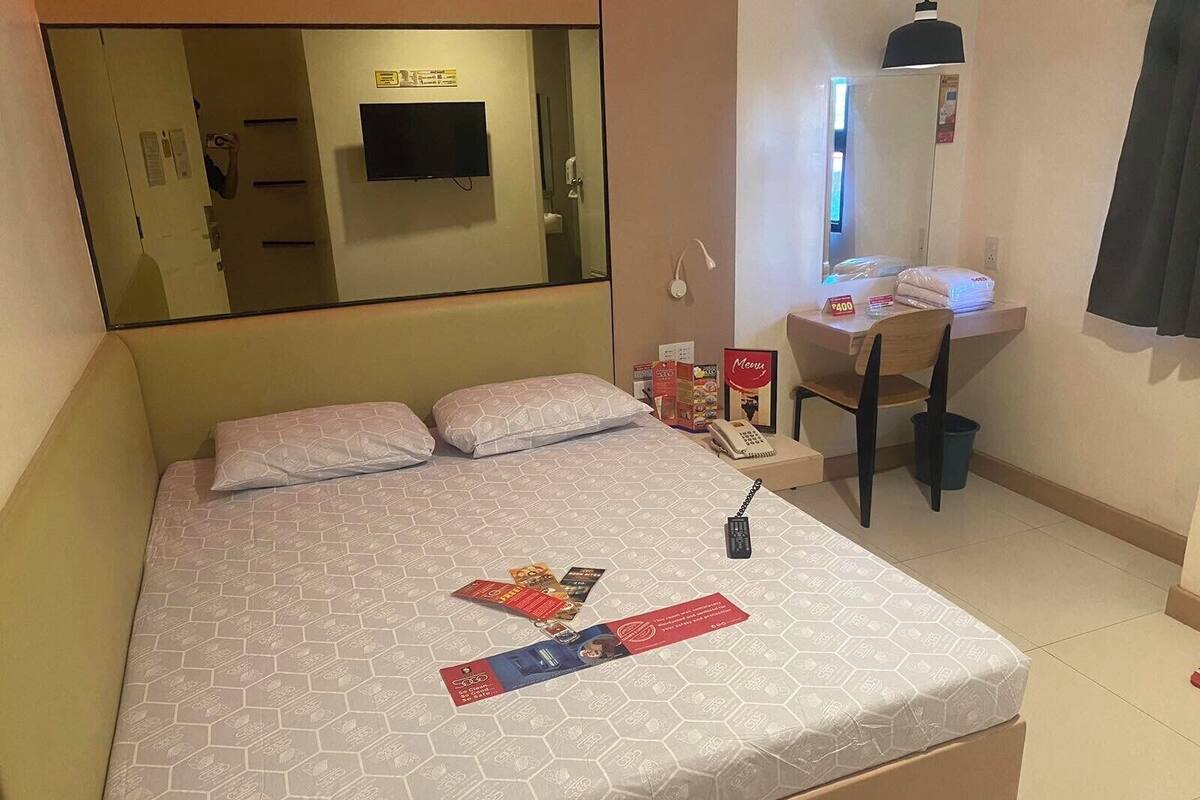 Una habitación de hotel con cama, escritorio, silla, teléfono y televisor.