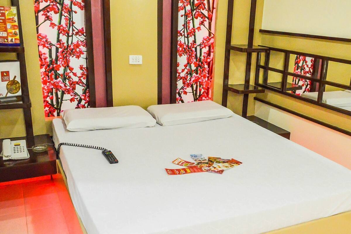 Habitación de hotel con una cama, una mesita de noche con un teléfono, una revista y una pared con estampado floral.