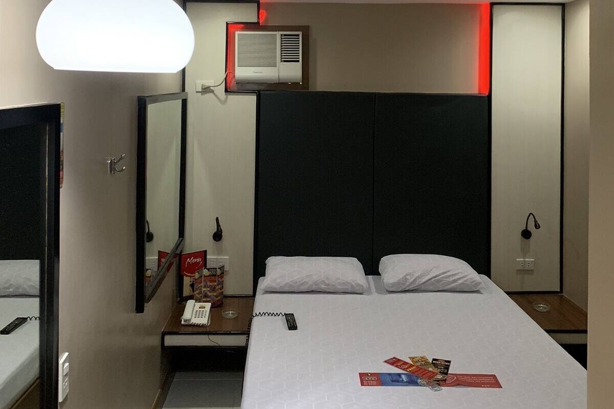 Habitación de hotel con cama, mesita de noche, espejo y lámpara en el techo.