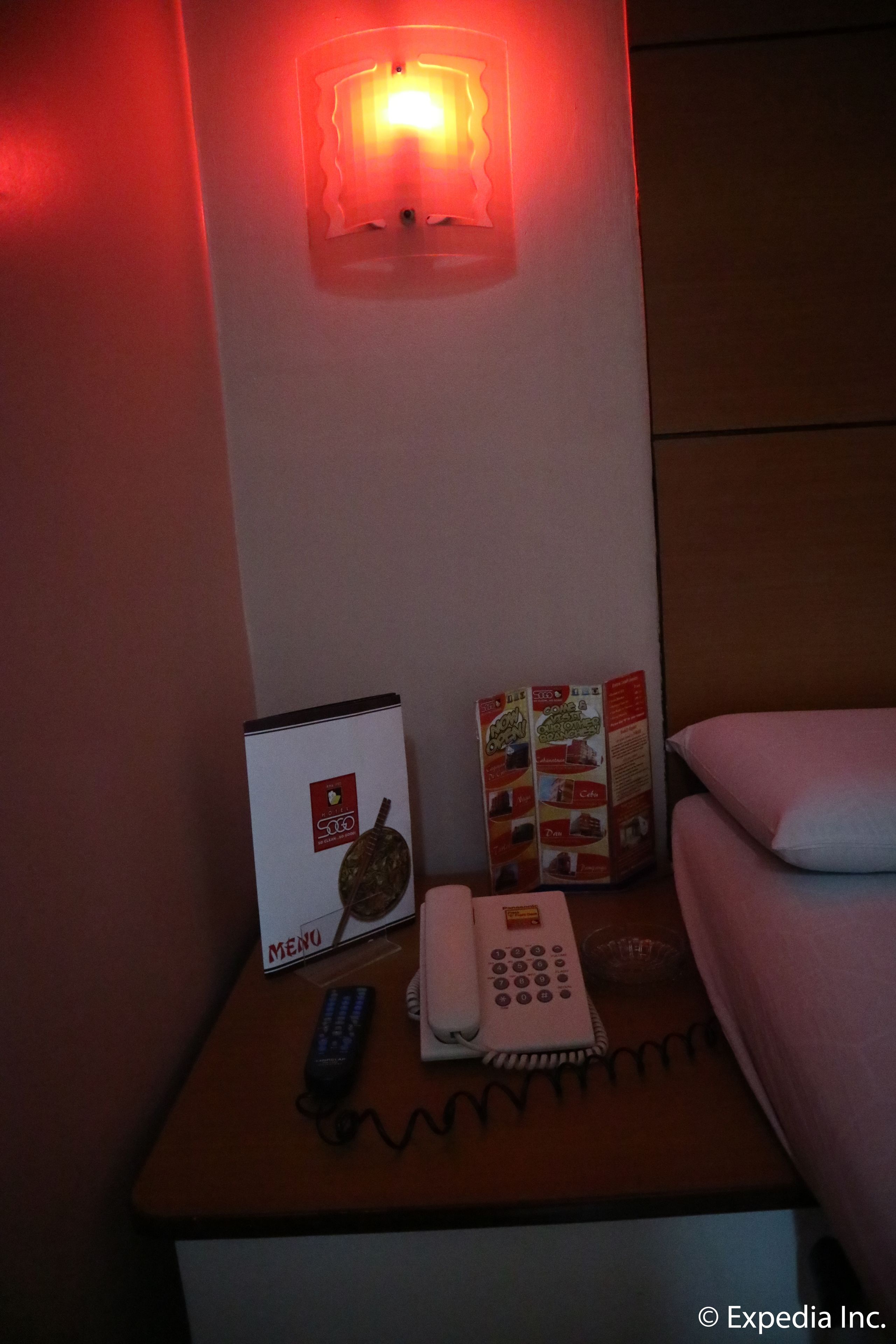 A hotel room with a bedside table featuring a menu, a telephone, and a remote control.
