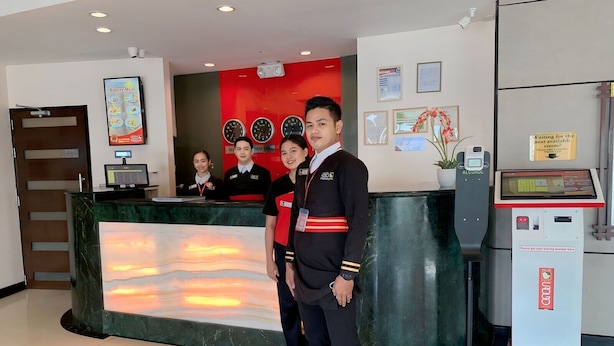 Zona de recepción de hotel con pantalla digital, reloj y señalización de área de espera.