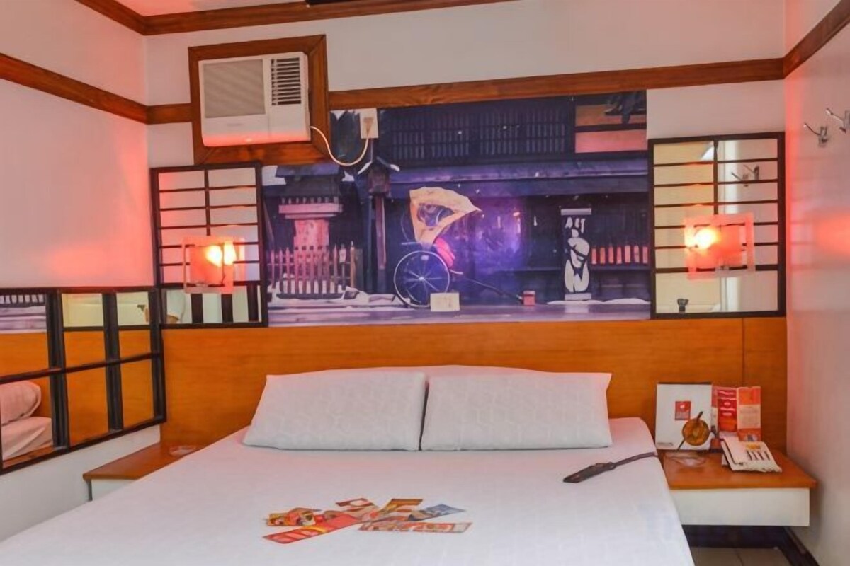 Habitación de hotel con cama, mesita de noche, aire acondicionado de pared y una pared decorativa con una bicicleta y una escena nocturna.