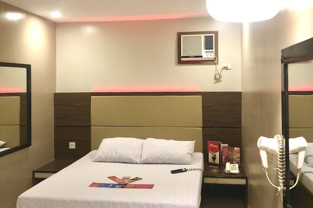 Una habitación de hotel con cama, mesita de noche y espejo.