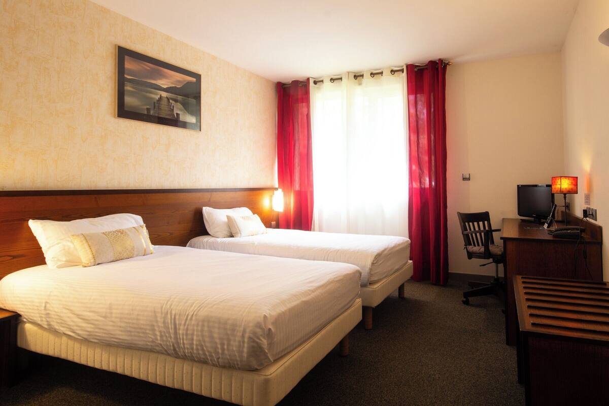 Een hotelkamer met twee bedden, een bureau, een stoel, een lamp en een schilderij aan de muur.
