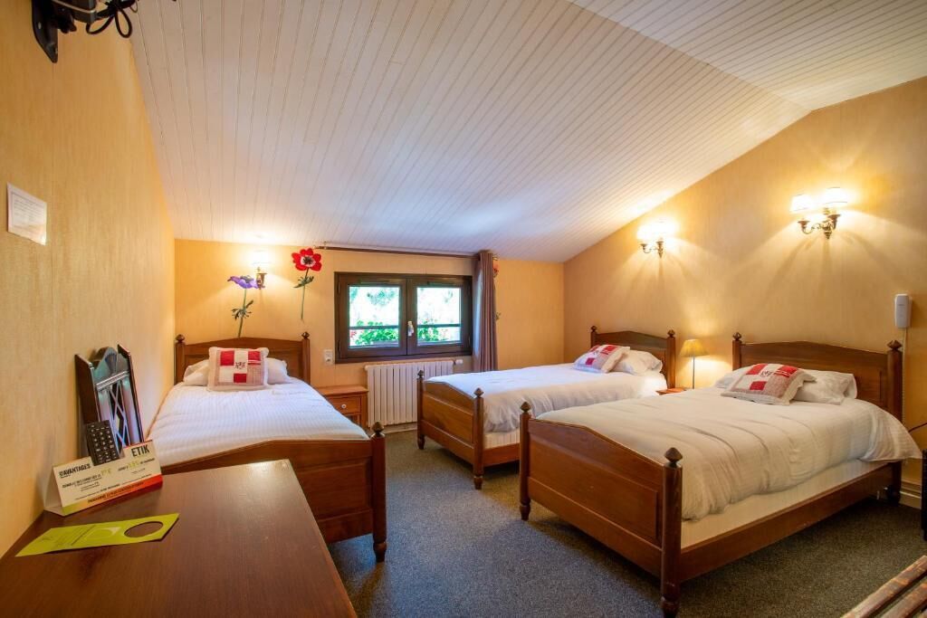 Une chambre d’hôtel avec deux lits en bois, une petite table avec un téléphone et une fenêtre donnant sur un paysage verdoyant.