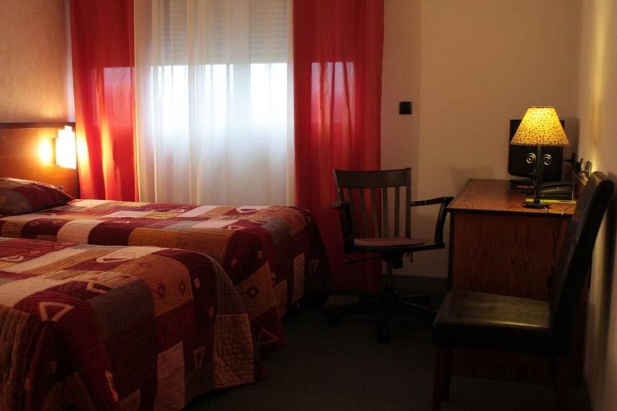 Een hotelkamer met twee bedden, een bureau met lamp en een stoel.