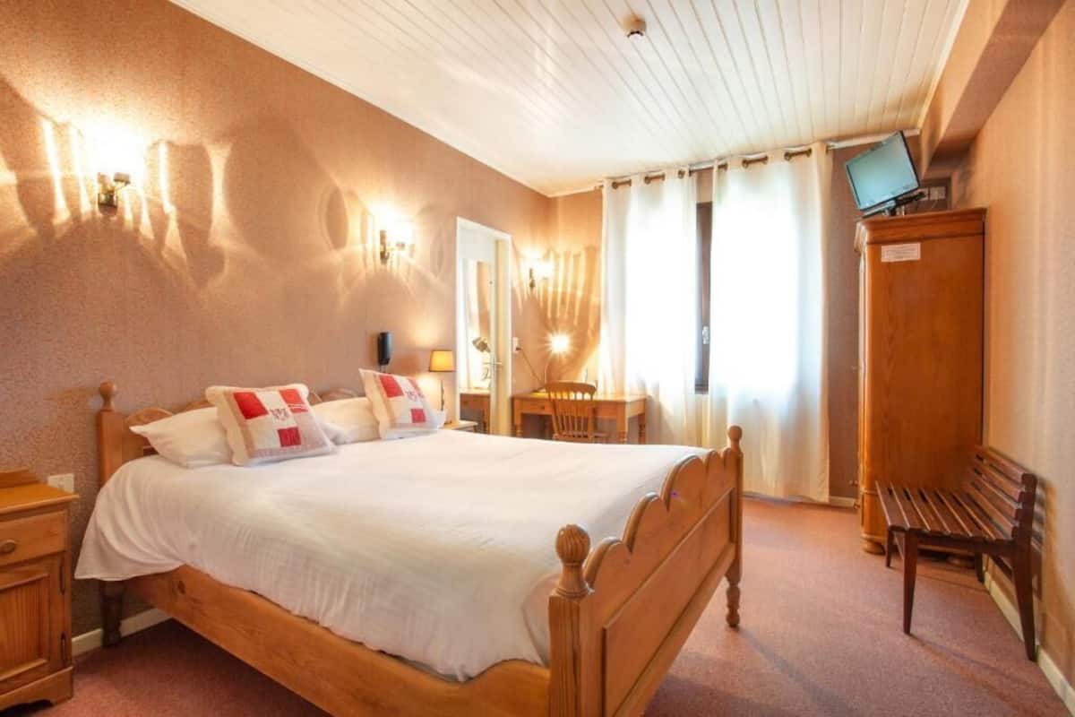 Een hotelkamer met een houten bed, nachtkastjes, een bureau, een stoel, een televisie en een kledingkast.