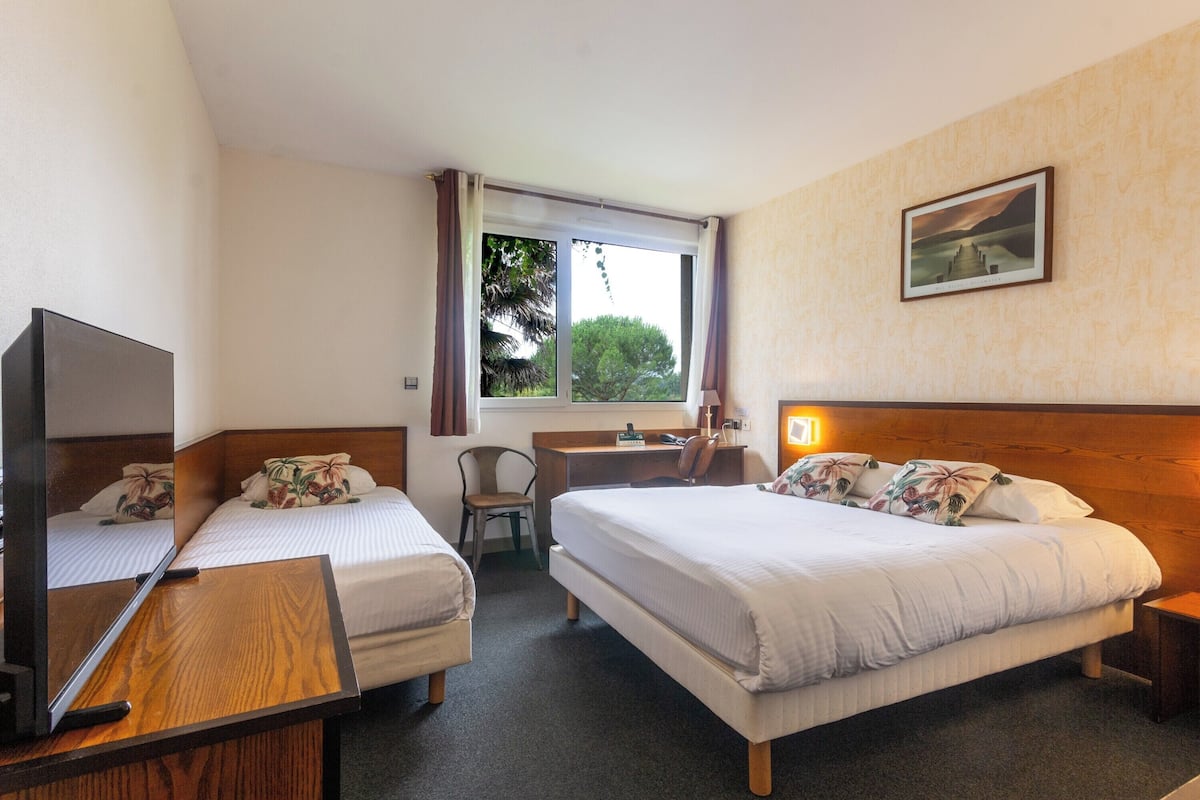 Een hotelkamer met twee éénpersoonsbedden, een bureau, een stoel, een televisie en een raam met gordijnen.