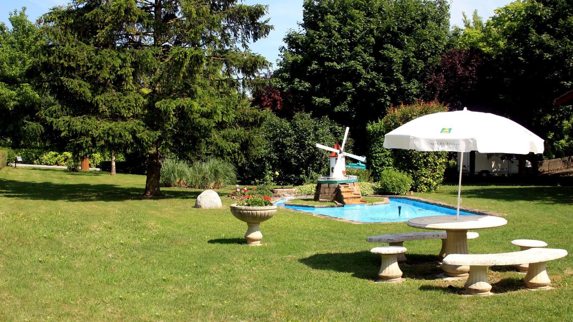 Un jardín con piscina, un molino de viento y mesas y bancos de piedra.