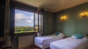 A room with two beds, a window with a view of the countryside, a radiator, and wall-mounted lights.
