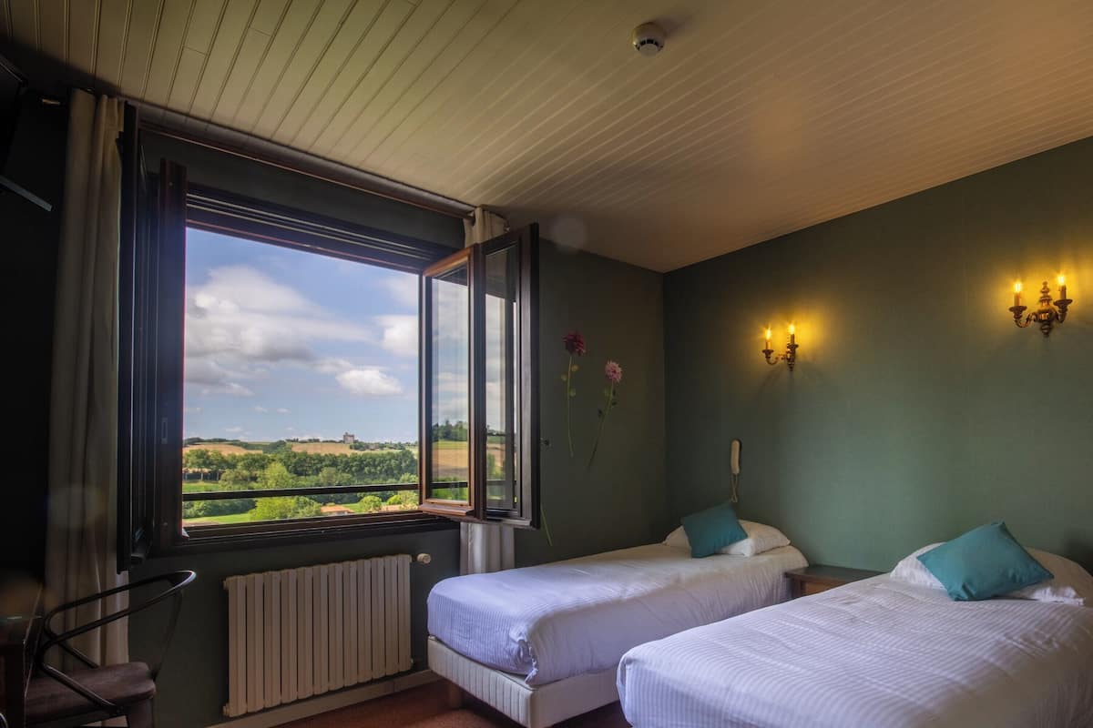 Een kamer met twee bedden, een raam met uitzicht op het landschap, een radiator en wandlampen.