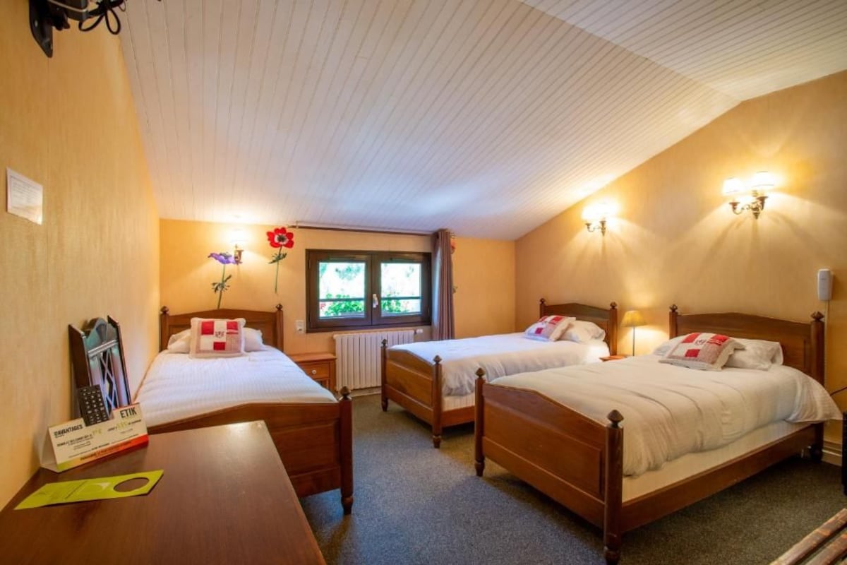 A hotel room with two wooden beds, a small table with a telephone, and a window with a view of greenery.
