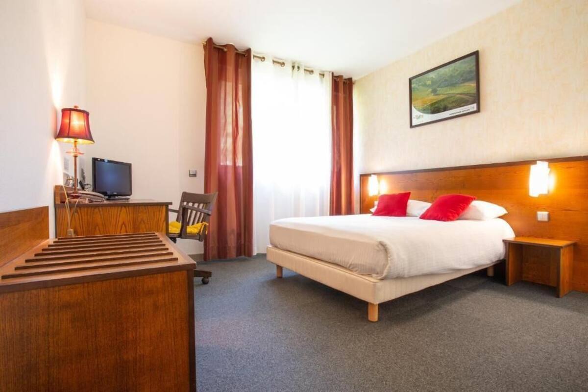 Een hotelkamer met een bed, een bureau met stoel, een televisie en een schilderij aan de muur.
