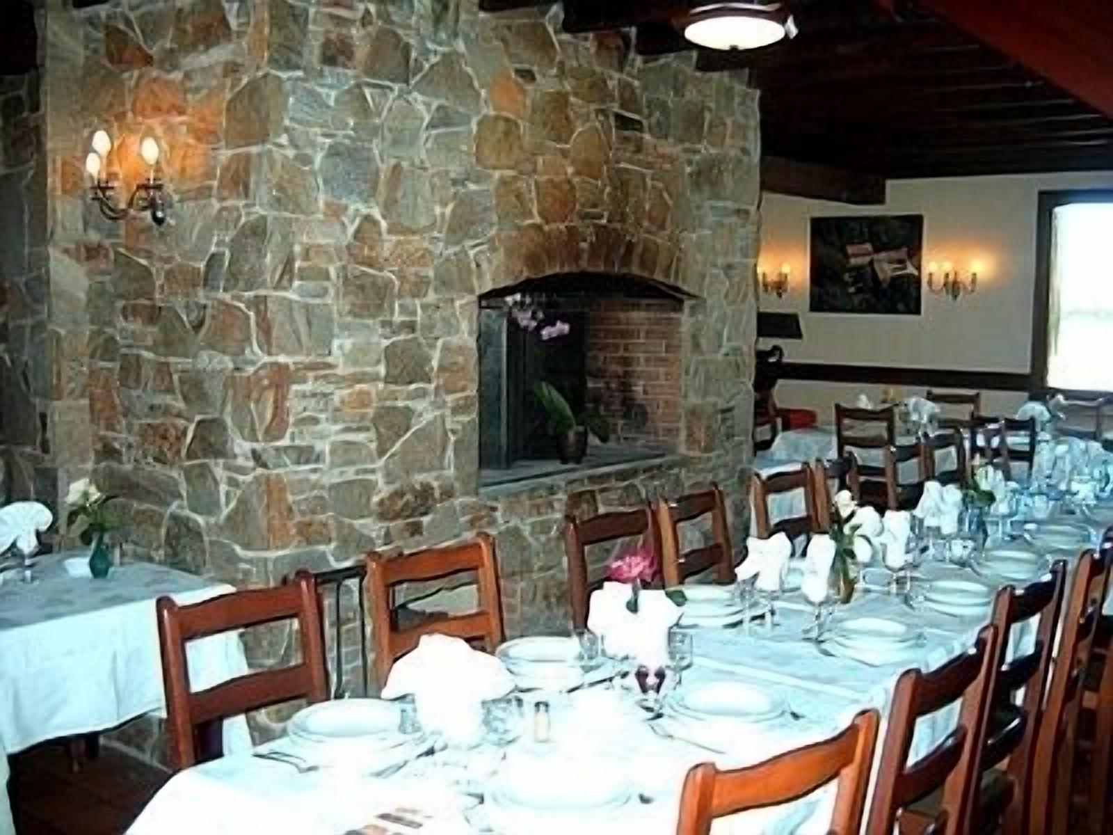 Un restaurant aux murs de pierre, doté d’une cheminée et de tables dressées pour le repas.