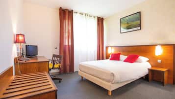Habitación de hotel con cama, escritorio con computadora, silla, lámpara y un cuadro en la pared.