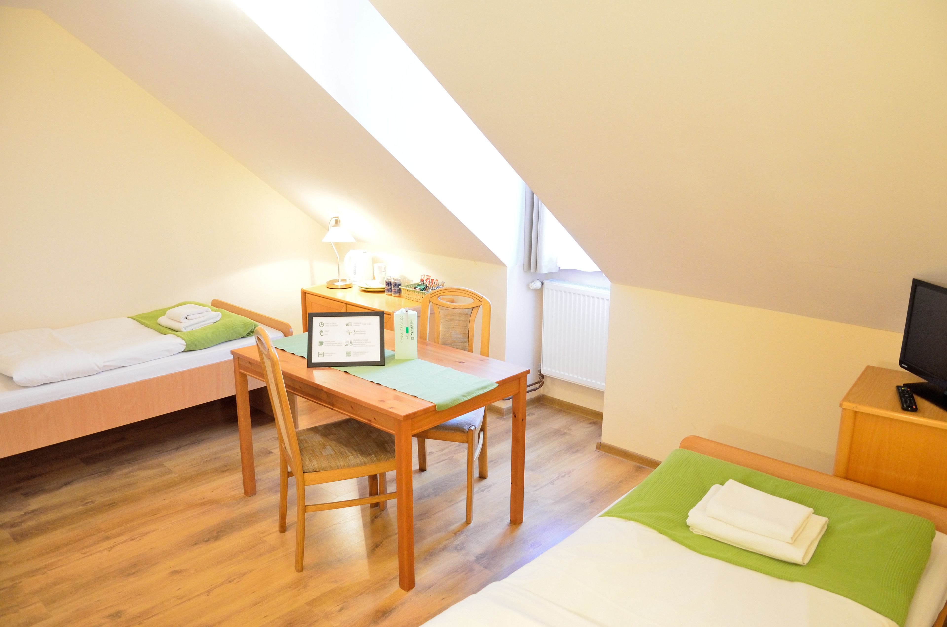 Een kleine, goed verlichte kamer met een bed, een bureau met een stoel, een lamp en een televisie.