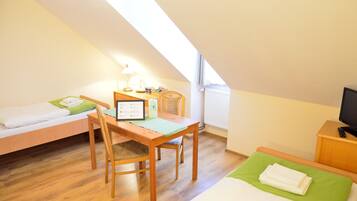 Een kleine, goed verlichte kamer met een bed, een bureau met een stoel, een lamp en een televisie.