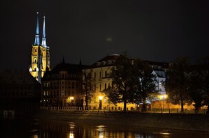 Vista nocturna de un edificio histórico con una torre destacada y un río al frente.