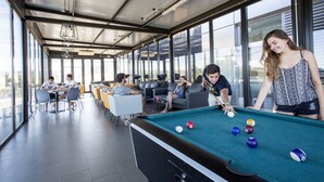 Una mesa de billar en un espacio interior moderno con amplios ventanales, zonas de estar y un área de comedor informal.